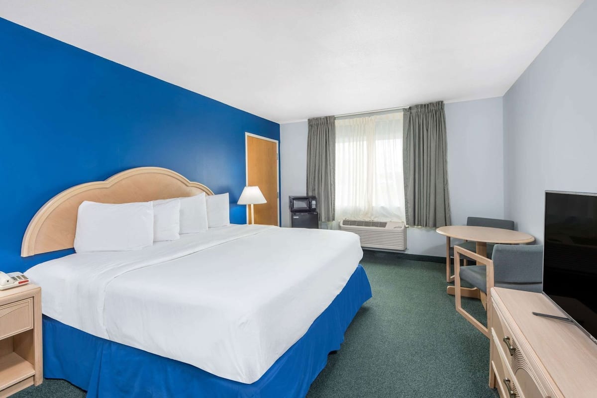 Ein Hotelzimmer mit einem Bett, einem Schreibtisch mit Stuhl, einem Fernseher und einem Fenster mit Vorhängen.