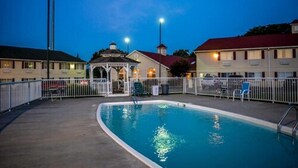 A swimming pool with a gazebo and lounge chairs, surrounded by a fence.