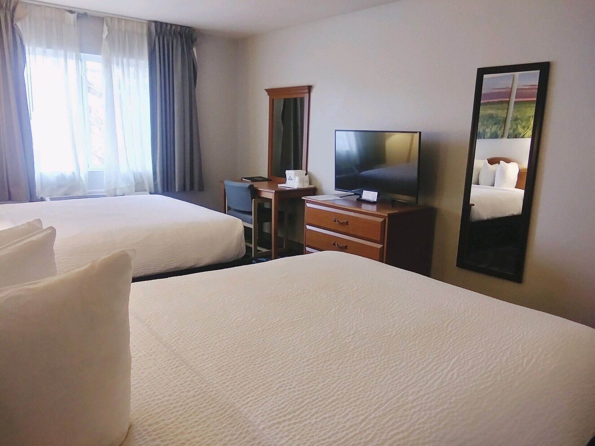 Habitación de hotel con dos camas, un escritorio con una computadora, un televisor y un espejo.
