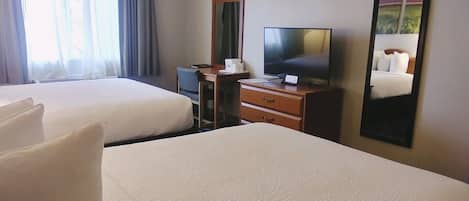 A hotel room with two beds, a desk with a computer, a television, and a mirror.