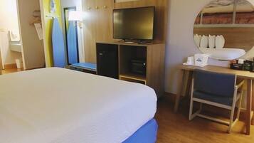 A hotel room with a large bed, a desk with a chair, a television, and a wardrobe.