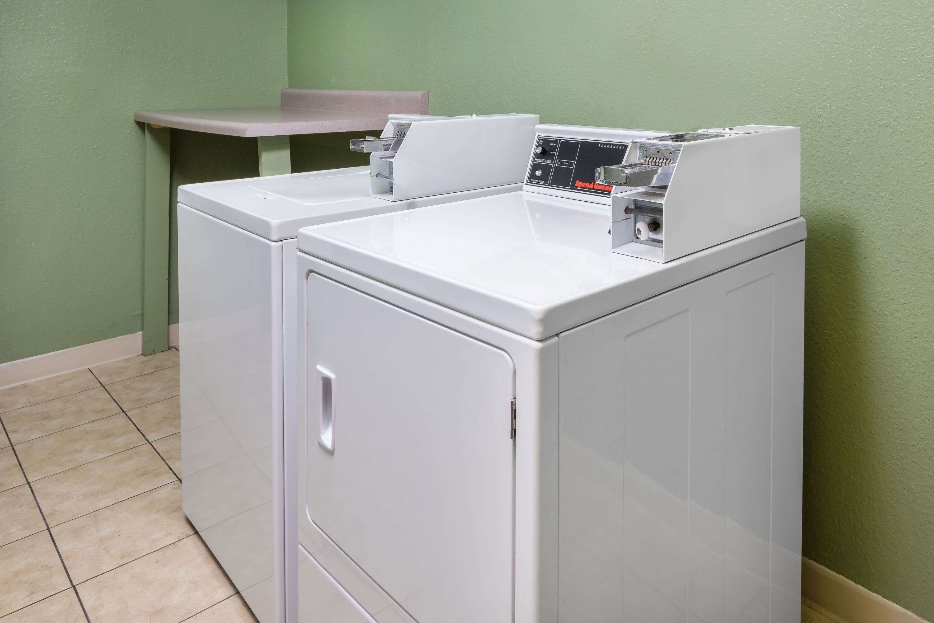 A compact laundry area with a front-loading washer and dryer, a small table, and a bench.