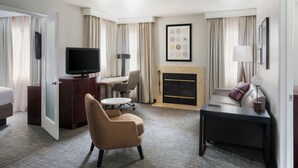 Ein Hotelzimmer mit Bett, Schreibtisch mit Flachbildfernseher, Sofa, Kamin und Essecke mit Stuhl und Tisch.