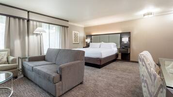 Una habitación de hotel con un sofá gris, una cama, una mesita de vidrio y una silla.