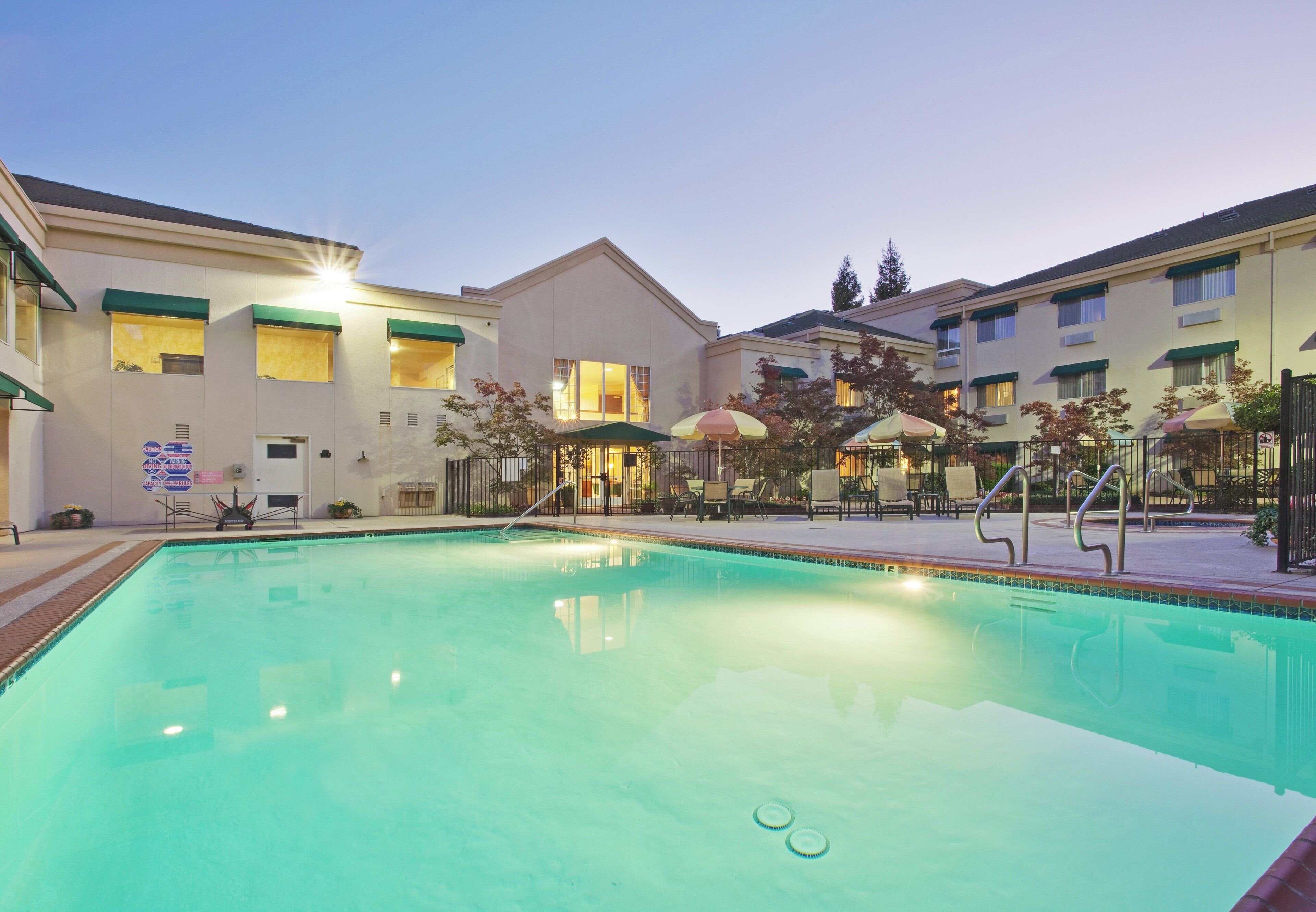 Un hotel con piscina, zona de estar exterior e iluminación en la entrada.