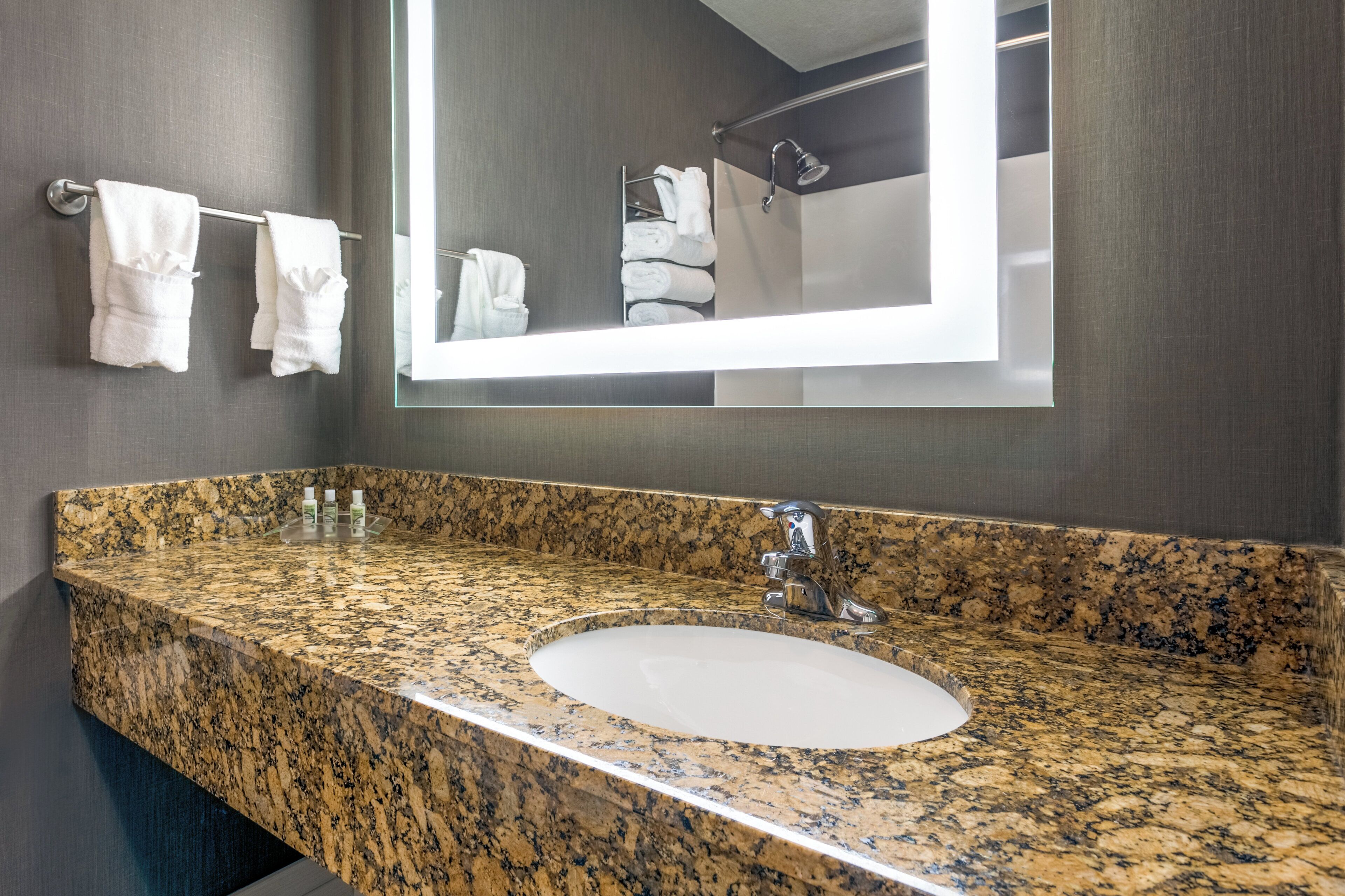 A bathroom with a granite countertop sink, a mirror, and a towel rack with folded towels.