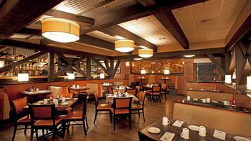 Interior de restaurante con vigas de madera, lámparas colgantes y una zona de bar.