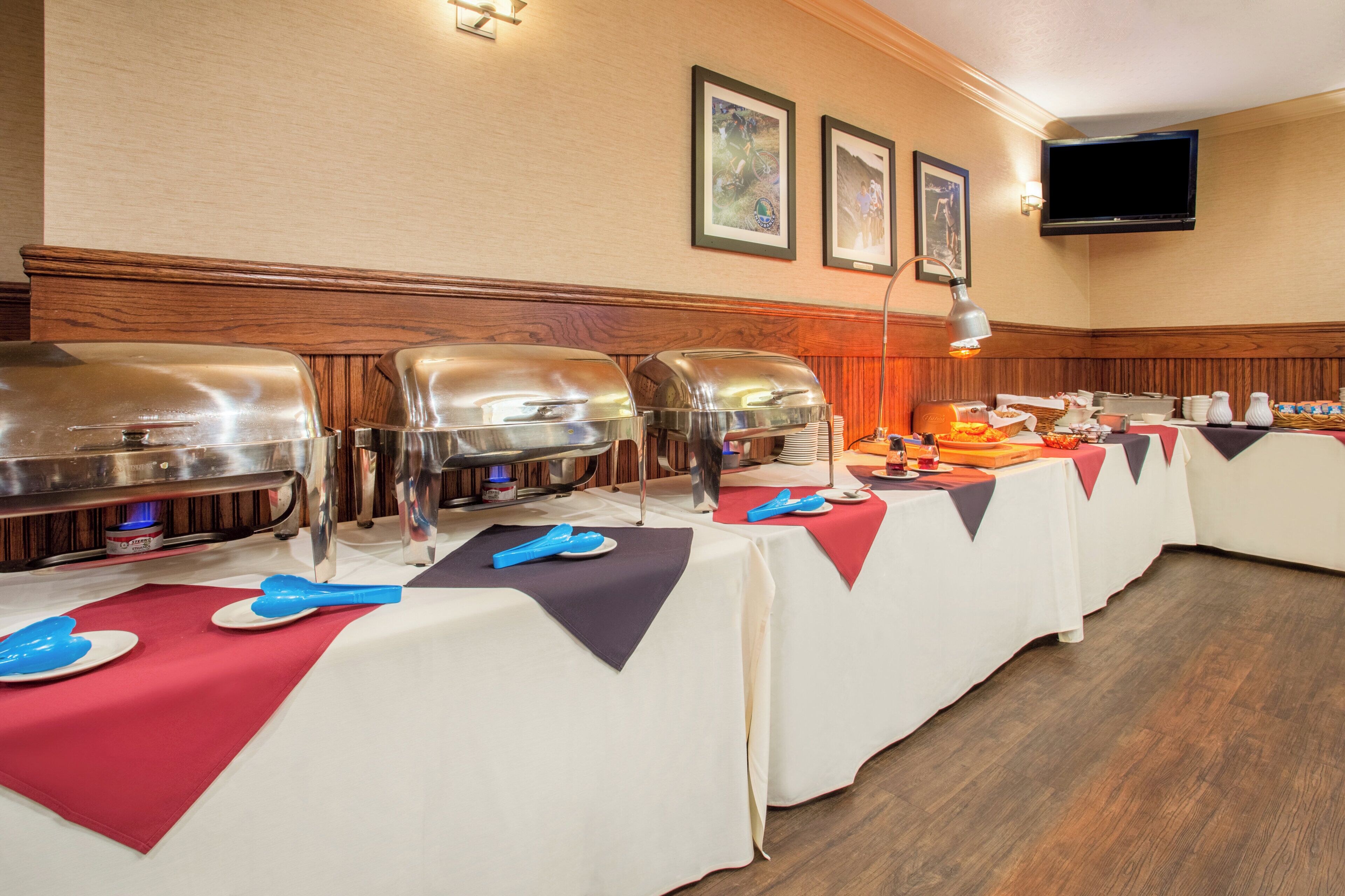 A buffet setup with multiple food service stations, a flat-screen TV mounted on the wall, and a wooden panel design on the wall.