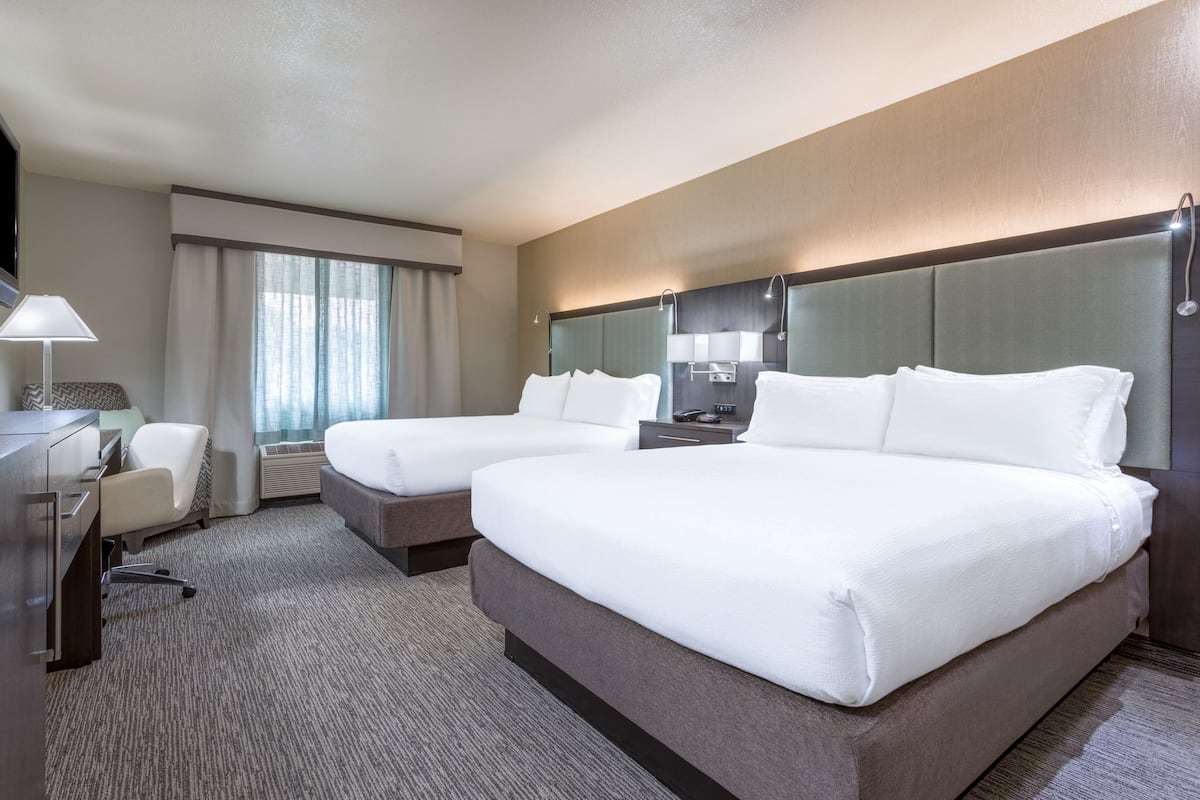 A hotel room with two beds, a desk, a chair, a TV, and a large window with curtains.