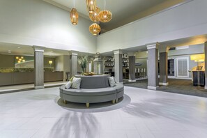 Un hall d’entrée spacieux avec un espace salon central, un comptoir d’accueil et un escalier menant aux étages supérieurs.