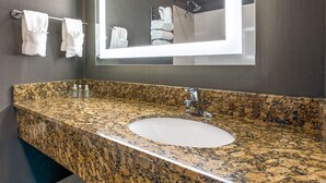 A bathroom with a granite countertop sink, a large mirror, and towels hanging on a rack. - Holiday Inn Auburn by IHG (Auburn)