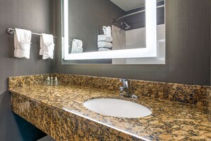 A bathroom with a granite countertop sink, a large mirror, and towels hanging on a rack. - Holiday Inn Auburn by IHG (Auburn)