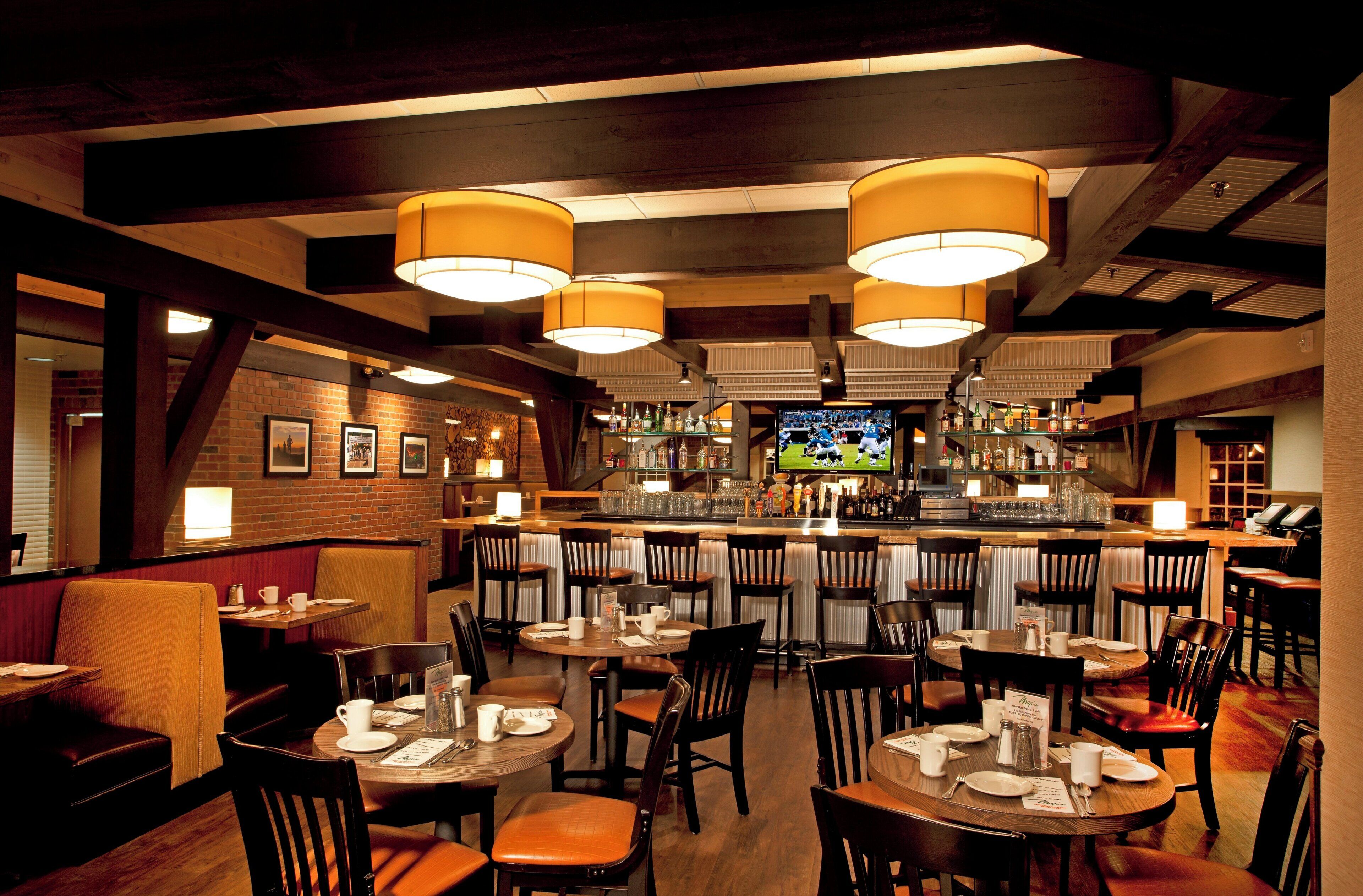 A restaurant with multiple tables and chairs, a bar area with a television, and a brick wall with framed pictures.