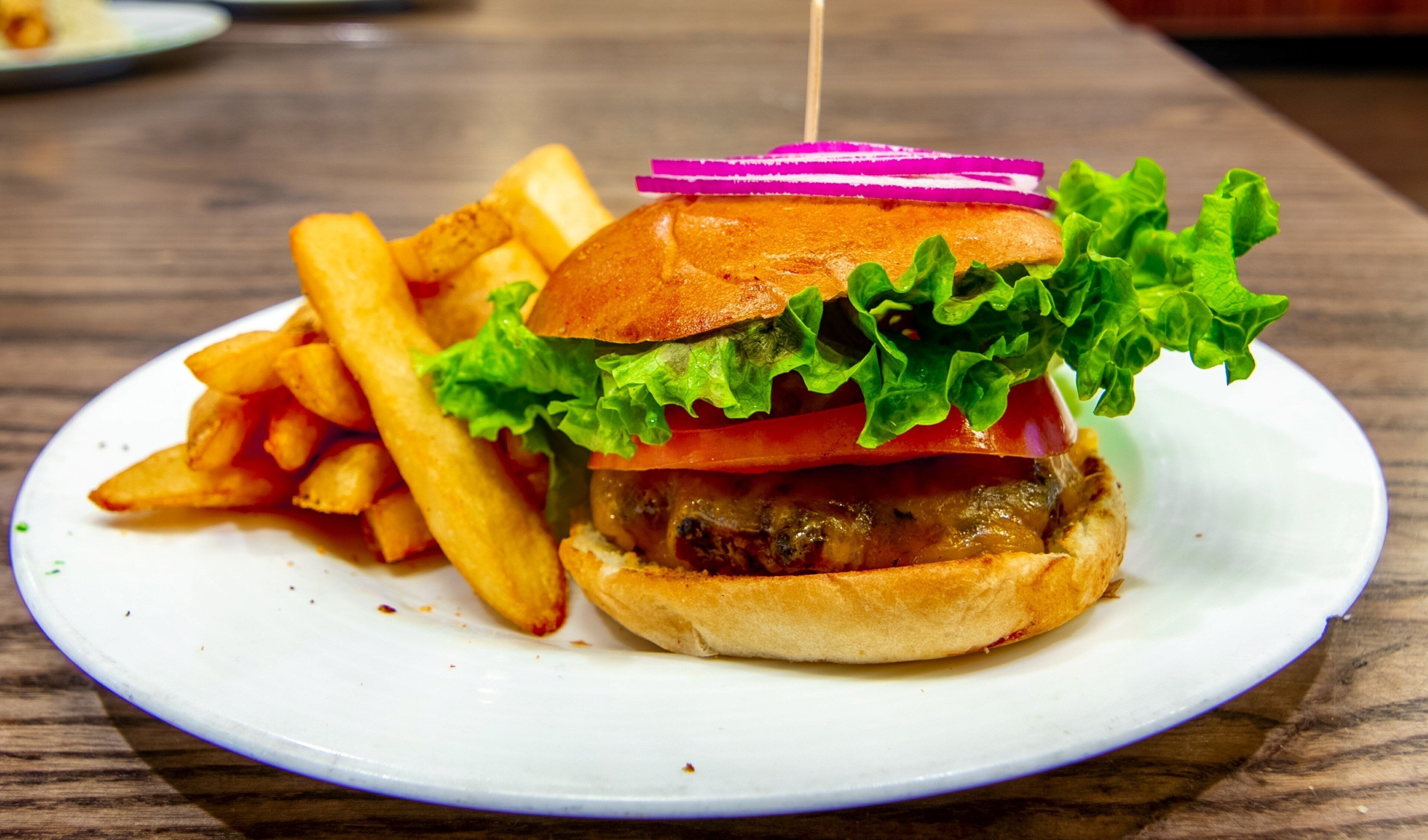 A burger with lettuce, tomato, and a bun, accompanied by a side of fries on a white plate.