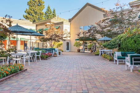 A courtyard with outdoor seating, a building entrance, and surrounding greenery.