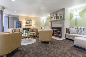 A hotel lobby with a fireplace, seating area, and a sign listing amenities. - Holiday Inn Auburn by IHG (Auburn)