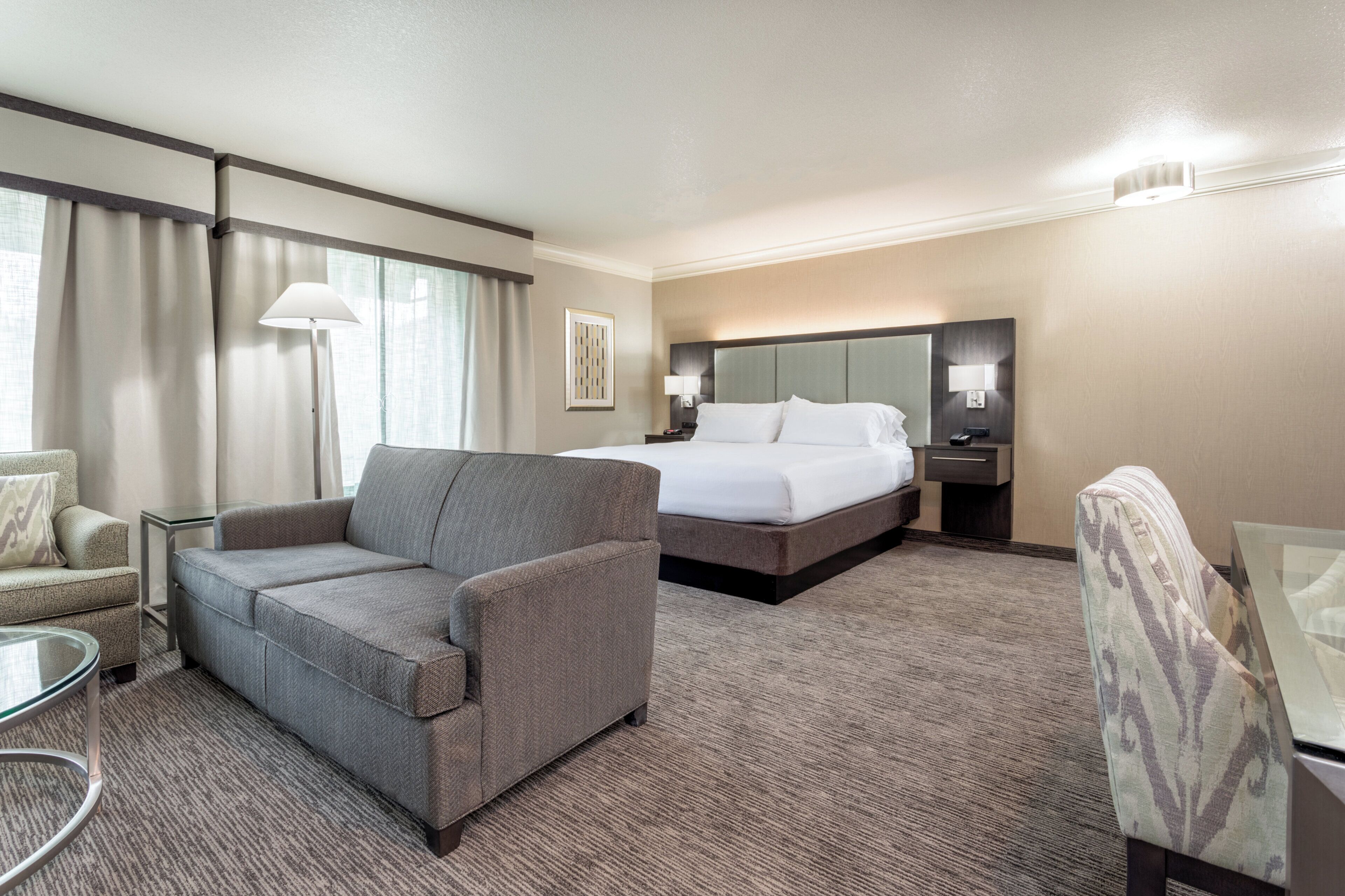 A hotel room with a bed, a sofa, a chair, a desk, and a lamp.