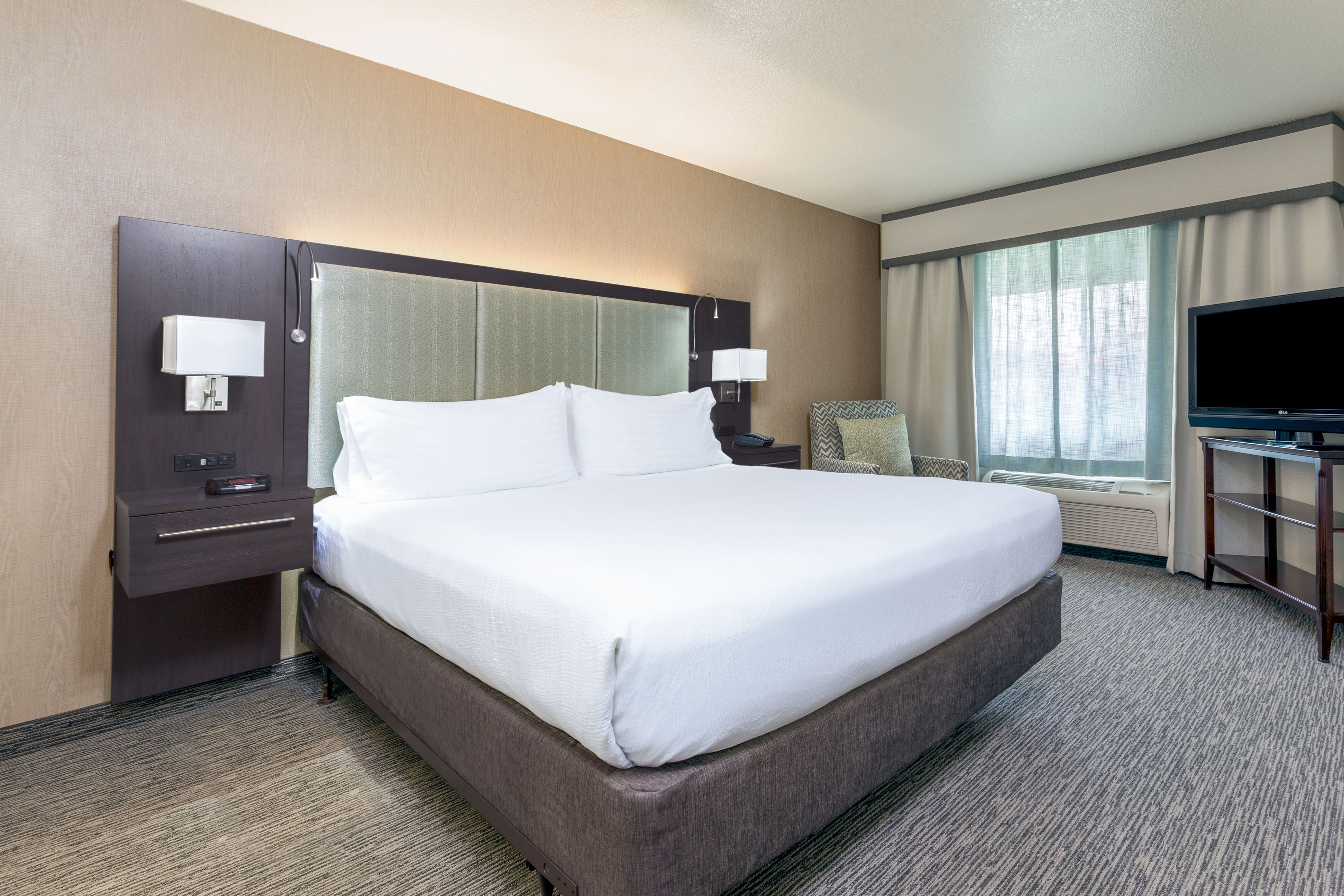 A hotel room with a large bed, a desk with a lamp, a television, and a window with curtains.