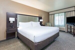 Habitación de hotel con una cama grande, un escritorio con lámpara, televisión y ventana con cortinas.