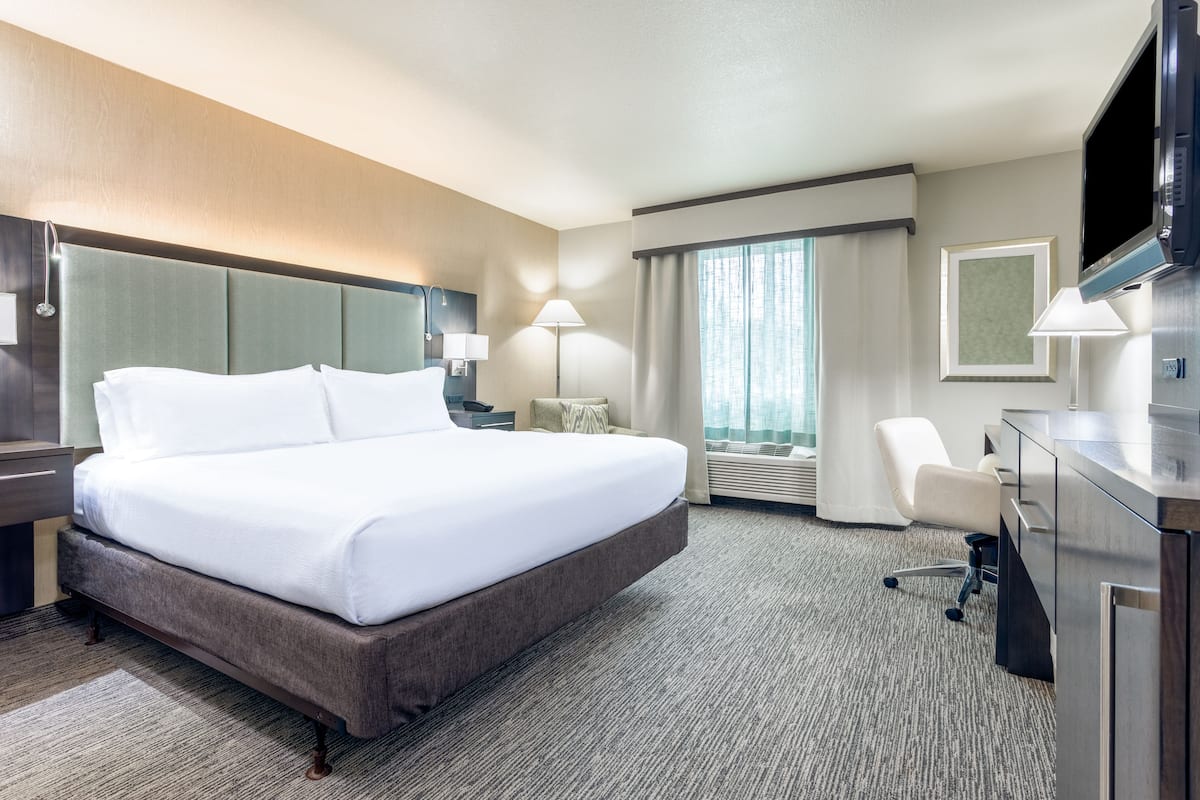 A hotel room with a large bed, a desk with a flat-screen TV, a chair, and a desk lamp.