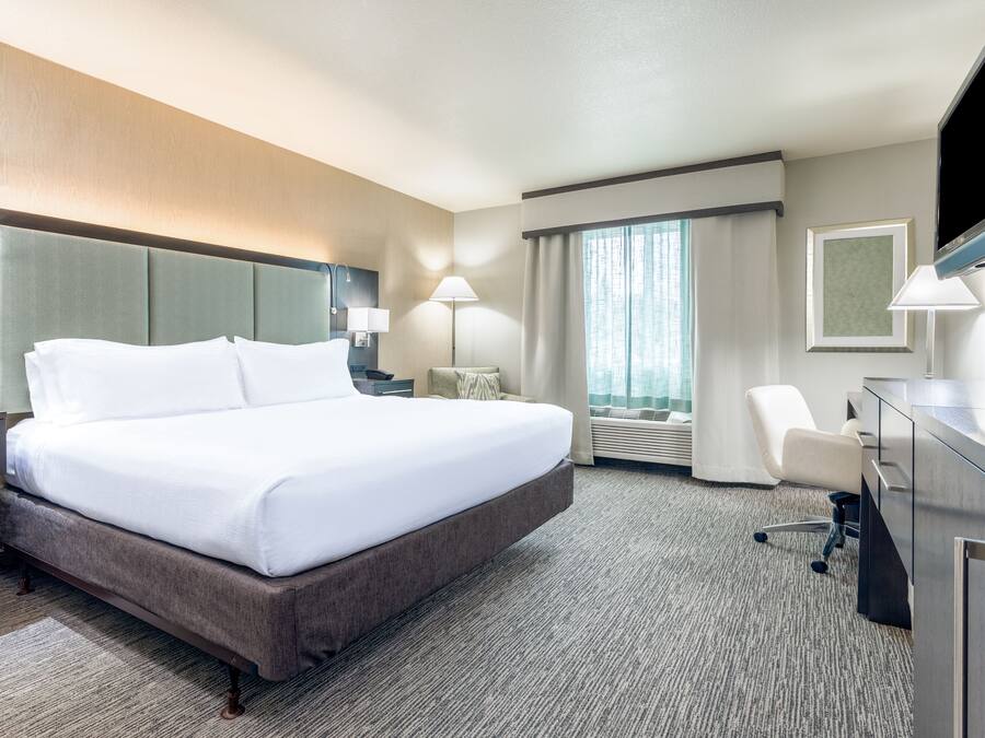 Ein Hotelzimmer mit einem großen Bett, einem Schreibtisch mit Flachbildfernseher, einem Sessel und einer Schreibtischlampe.