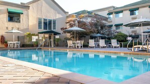 A swimming pool with lounge chairs and umbrellas, surrounded by buildings with balconies and windows.