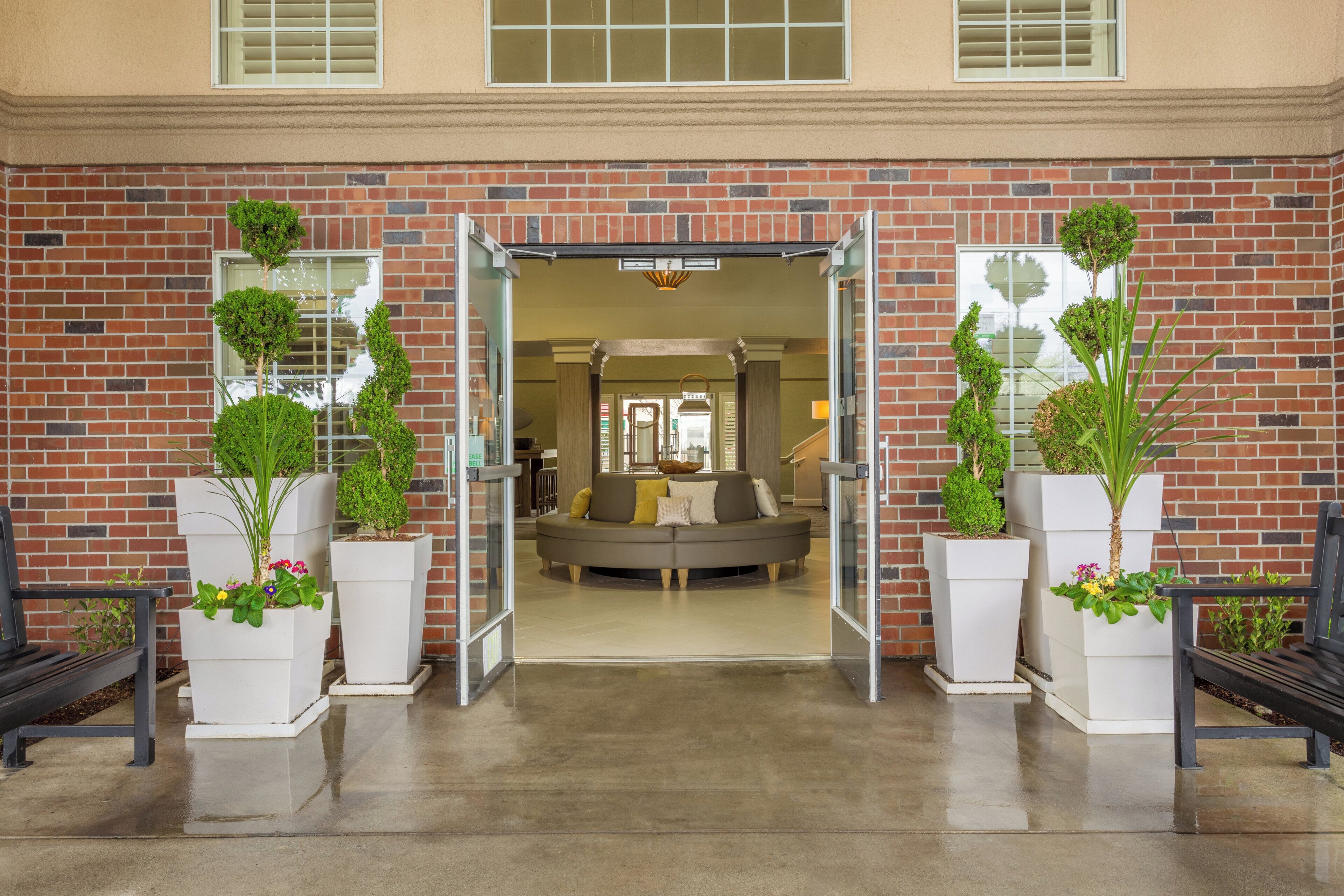 A brick building entrance with a glass door, a sofa, and potted plants.