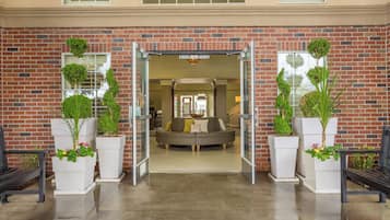 A brick building entrance with a glass door, a sofa, and potted plants.