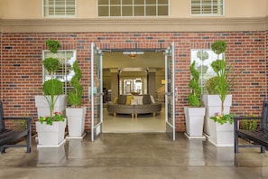 A brick building entrance with a glass door, a sofa, and potted plants.