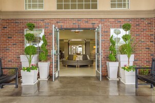 Entrada de un edificio de ladrillo con puerta de cristal, un sofá y plantas en macetas.