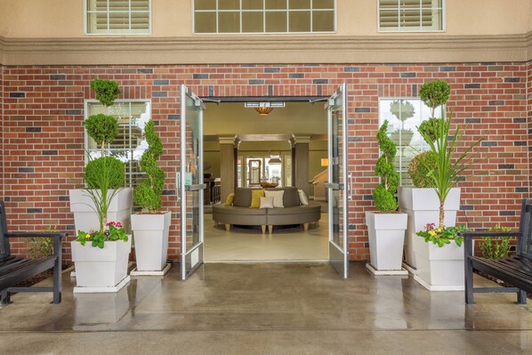 Entrada de un edificio de ladrillo con puerta de cristal, un sofá y plantas en macetas.