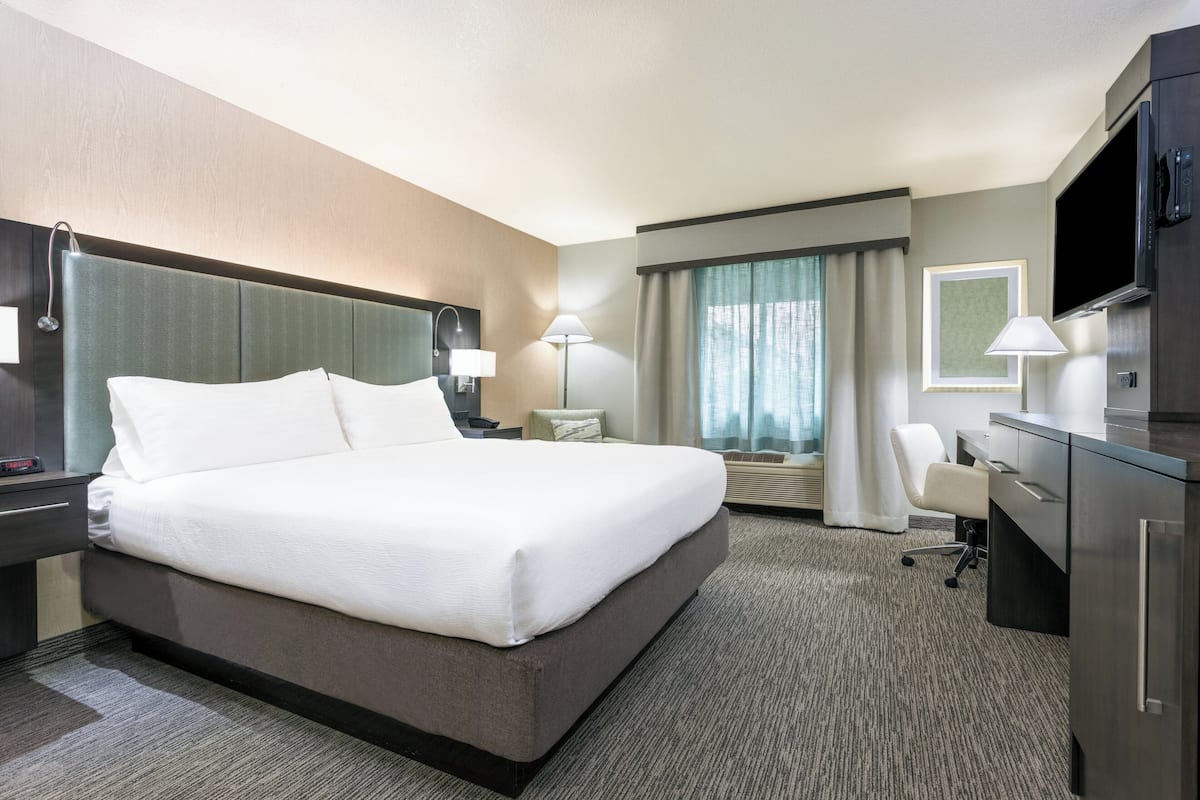 A hotel room with a large bed, a desk, a chair, a TV, and a window with curtains.