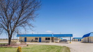 Un motel con techo azul, estacionamiento y un árbol en primer plano.