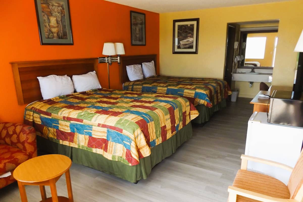 A hotel room with two beds, a desk, a chair, and a small table.