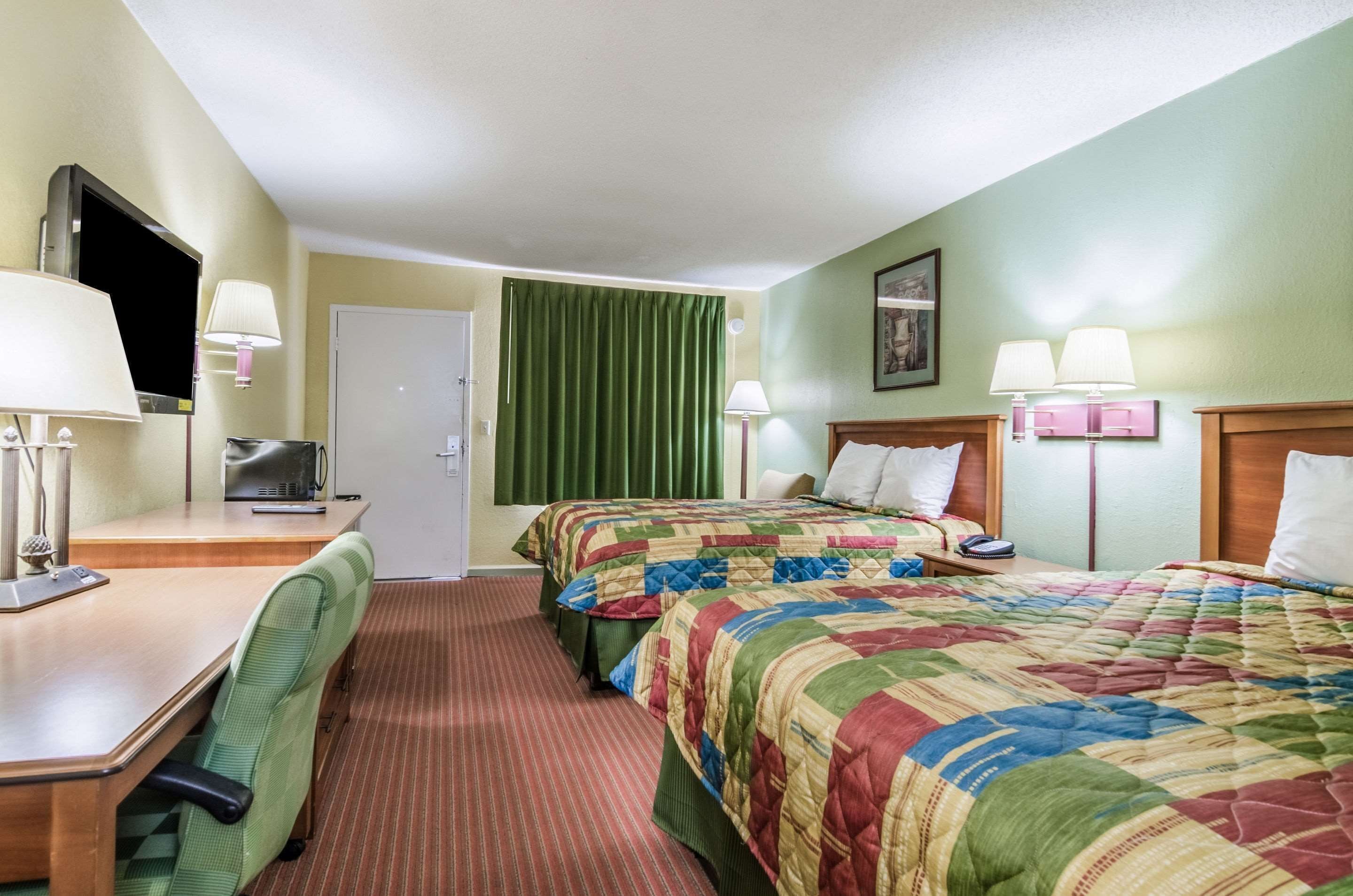 Ein Hotelzimmer mit zwei Betten, einem Schreibtisch, einem Sessel, einem Fernseher und einer Tür.