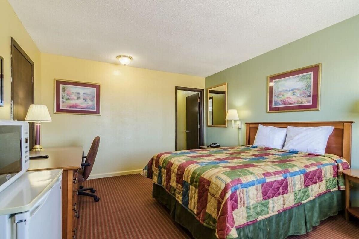 A hotel room with a bed, a desk, a chair, a television, and two framed pictures on the walls.