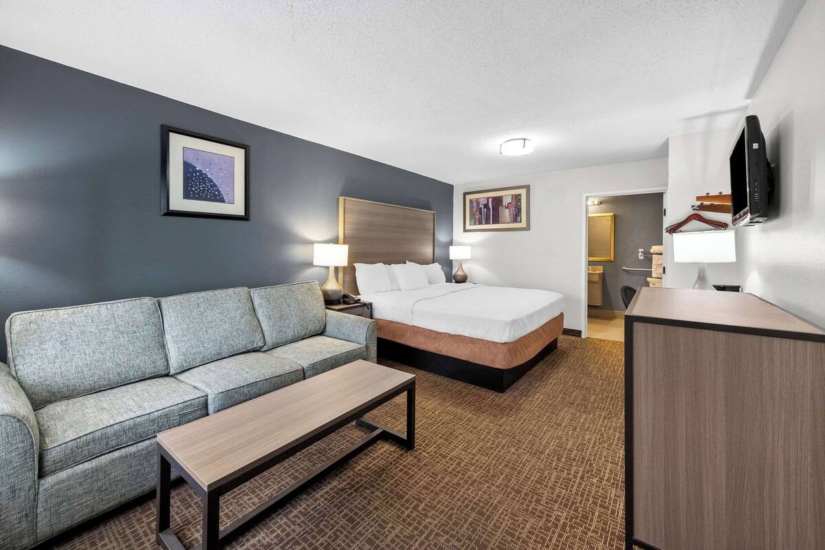 A hotel room with a bed, a sofa, a coffee table, and a desk.