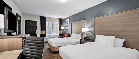 A hotel room with two beds, a desk with a computer, a chair, and a TV.