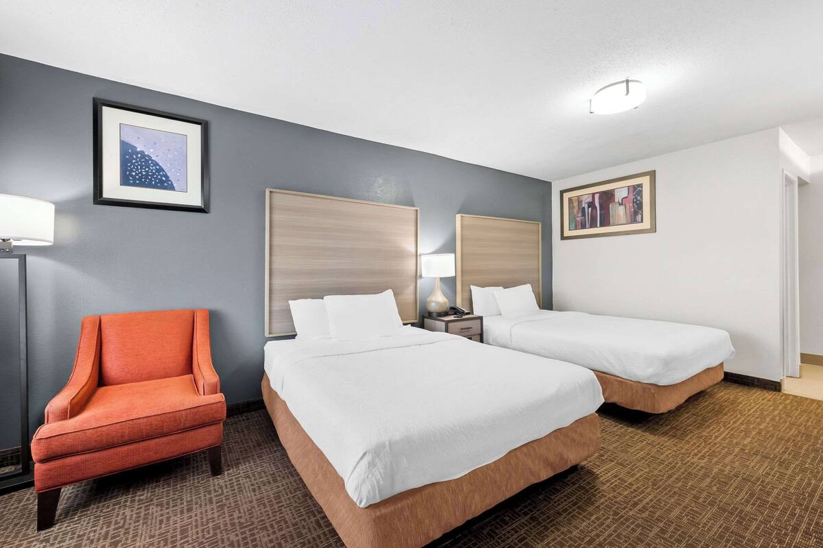 A hotel room with two beds, a chair, and artwork on the walls.