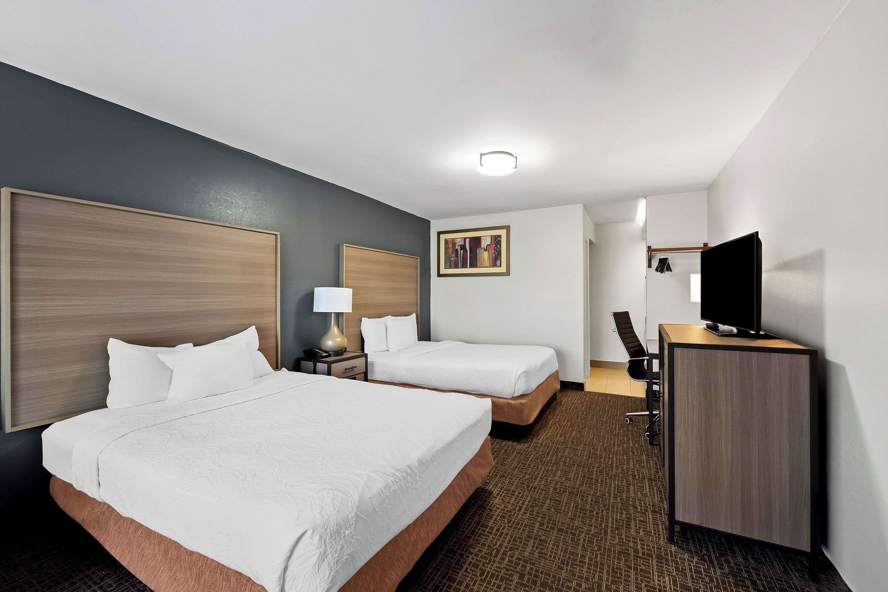 A hotel room with two beds, a desk, a television, and a painting on the wall.