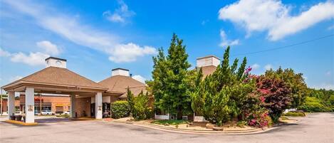 A hotel with a covered parking area, multiple chimneys, and landscaped gardens with various trees and shrubs.