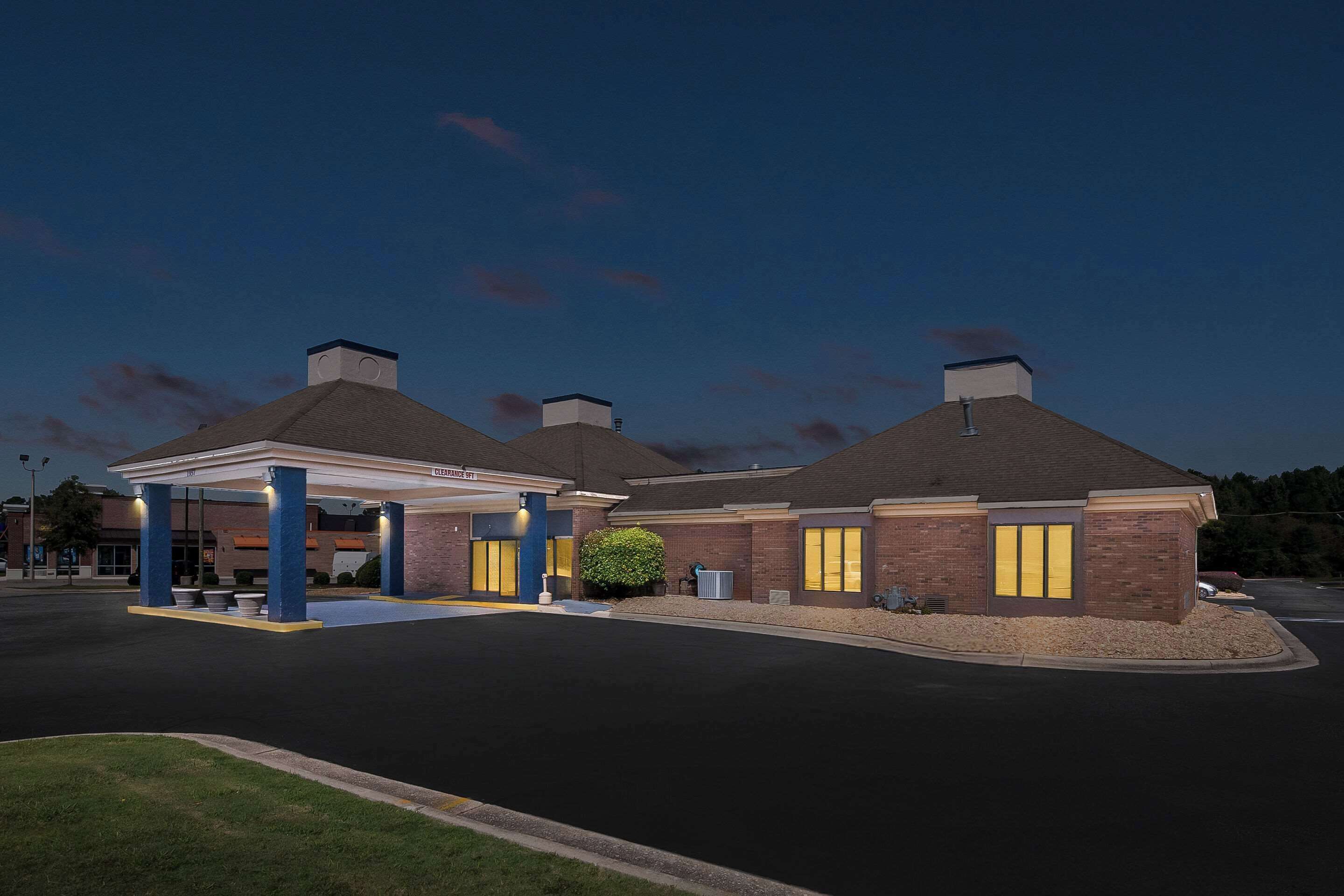 A hotel with a gas station, featuring a covered parking area, brick exterior, and a well-lit entrance.