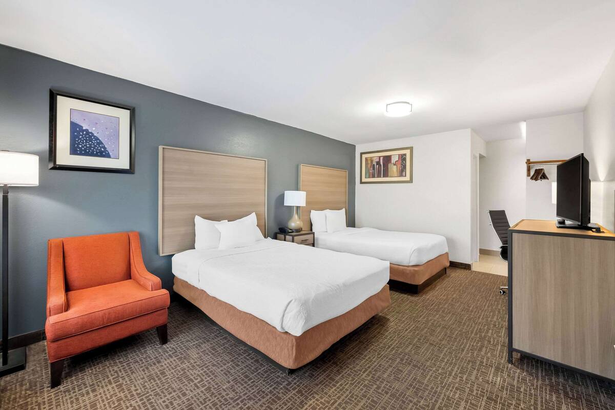 A hotel room with two beds, a desk, a TV, and a chair.