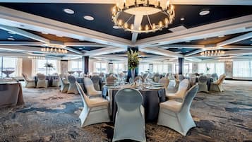 A banquet hall with round tables, chairs, and a central chandelier.