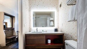 A bathroom with a wooden vanity, a large mirror, a toilet, and a shower area. - Holiday Inn Grand Haven-Spring Lake by IHG (Spring Lake)