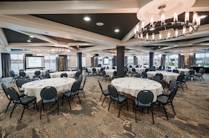 A large conference room with round tables and chairs, a projector screen, and a view of the water outside.