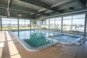 An indoor swimming pool with clear glass walls, a hot tub, and a view of the outside.
