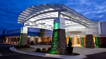 A hotel entrance with a modern design, featuring a curved glass canopy and stone pillars.
