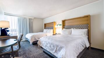 A hotel room with two beds, a desk, a chair, a lamp, and a window with curtains.
