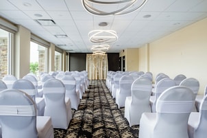 Un salón de conferencias con filas de sillas blancas, una alfombra estampada y una lámpara de techo moderna.